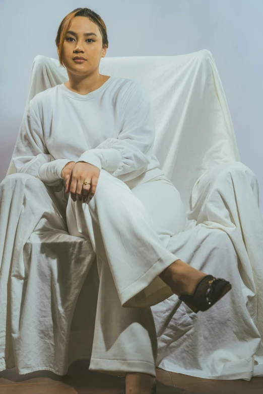 a woman sitting on a white chair in a white cloth dress