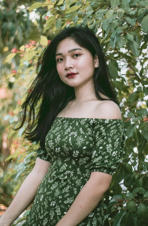 a woman posing by some trees wearing a green dress