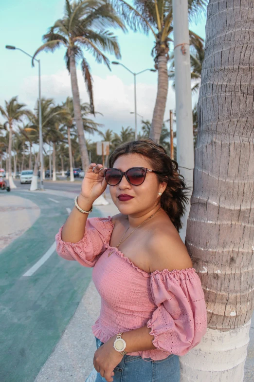 a young woman standing next to a palm tree on the street