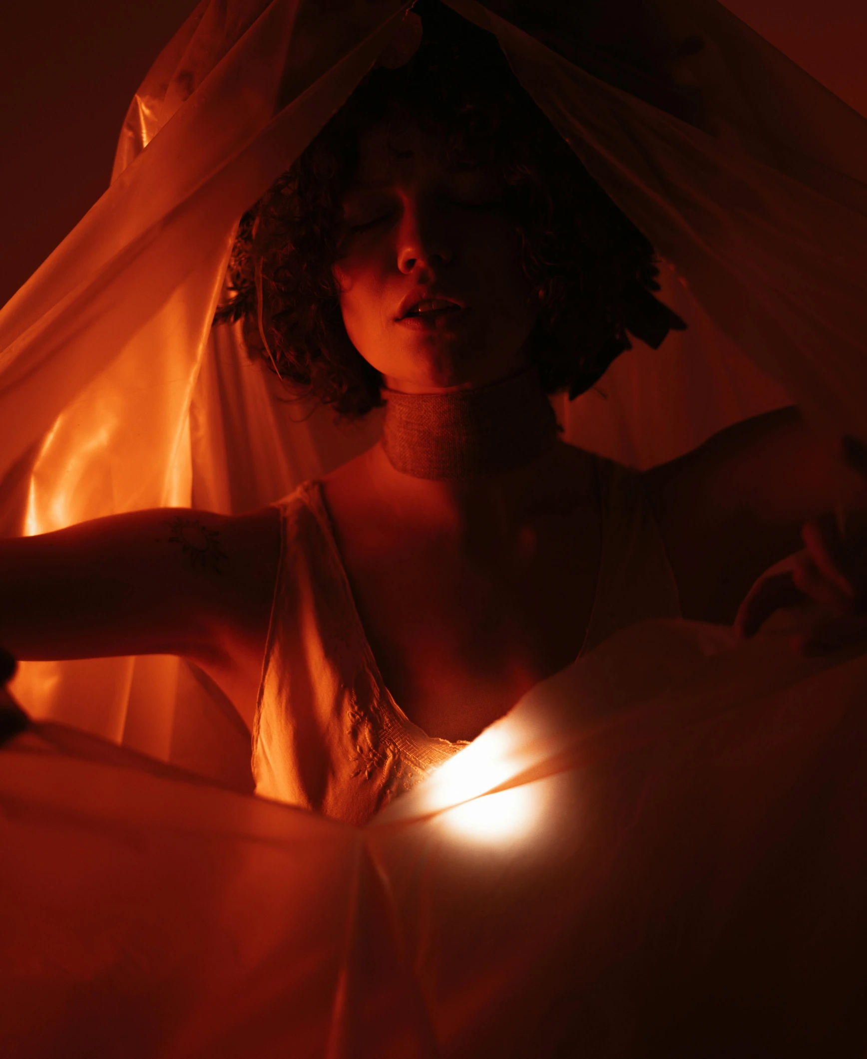 a woman in a red and yellow costume, hiding behind a sheered cloth