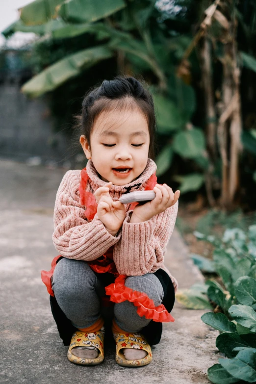 a little girl squatting with a cell phone in her hand