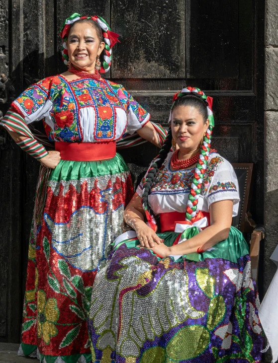 two women in colorful attire sit together on a bench