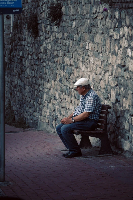 a man is sitting on a bench by a wall