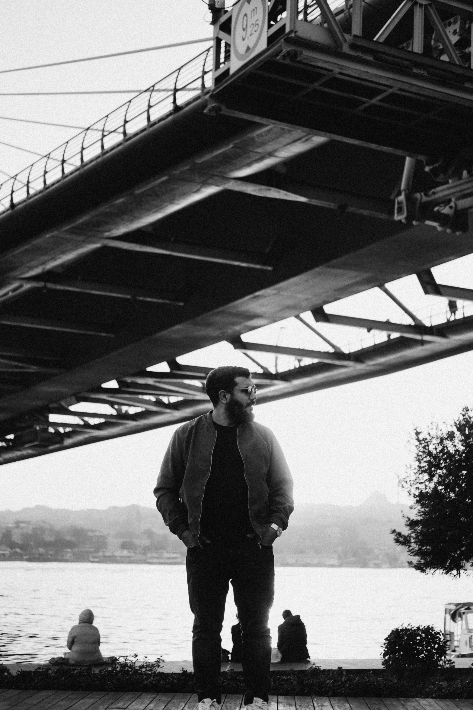 a man with a long beard standing on the water next to a bridge