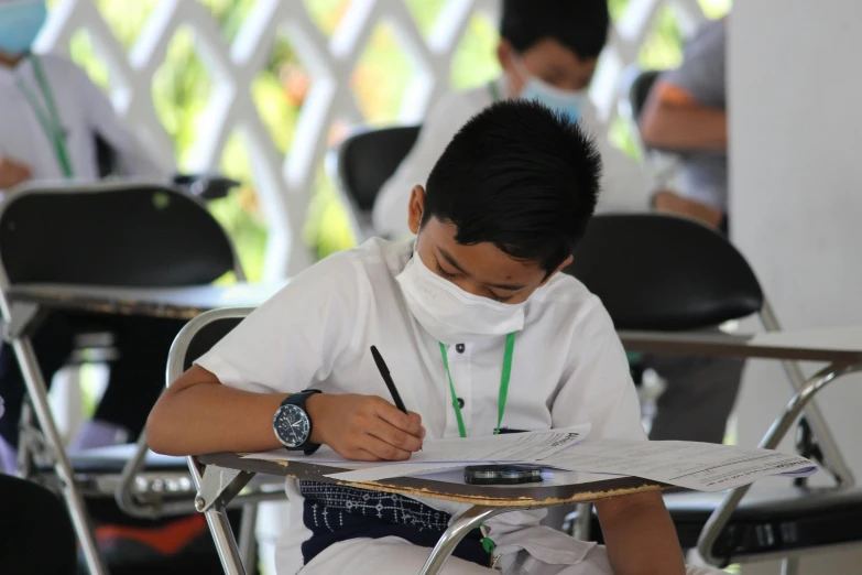 a young man wearing white clothes writing on paper