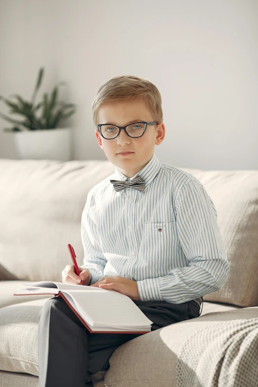 a boy sitting on a couch writing in his book