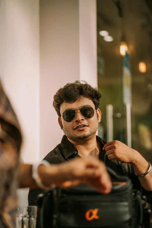 a man in sunglasses holds his bag while he is pointing at a woman