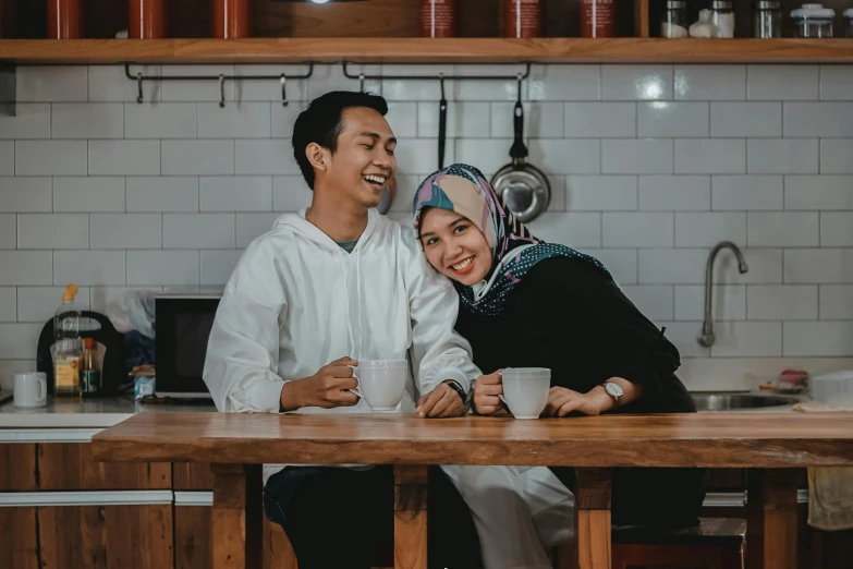 a couple sit together in the kitchen smiling for the camera