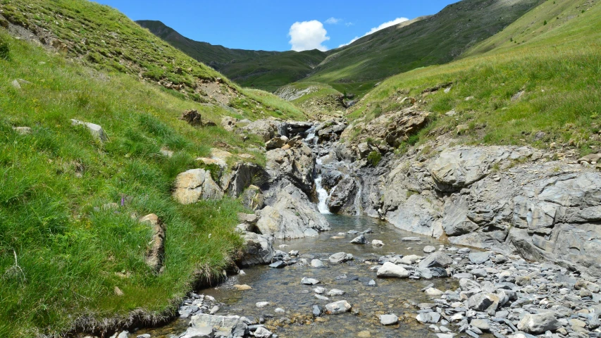 a stream running through an open valley, near green mountains