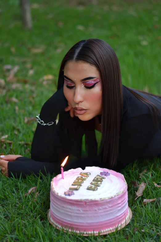 a woman lays on the grass while staring at a birthday cake