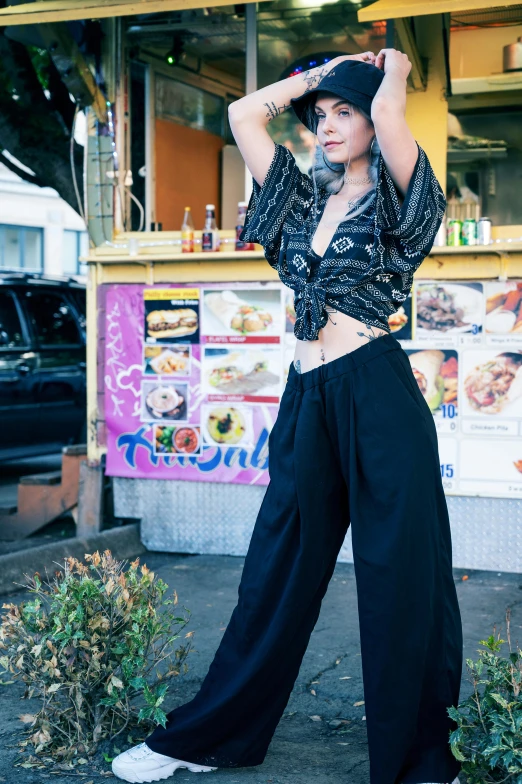 young woman standing on the sidewalk while holding her hat over her head