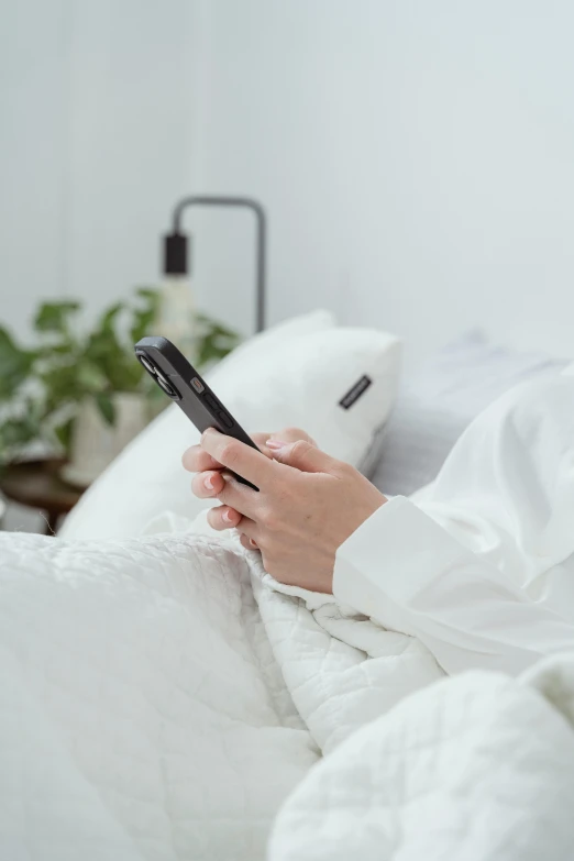 a woman in white and black clothes laying in bed looking at her phone