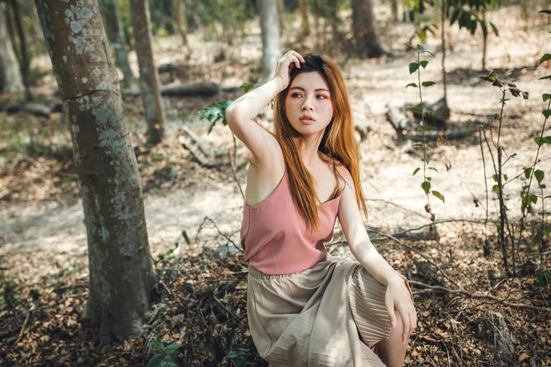 a woman with red hair sitting on the ground near some trees