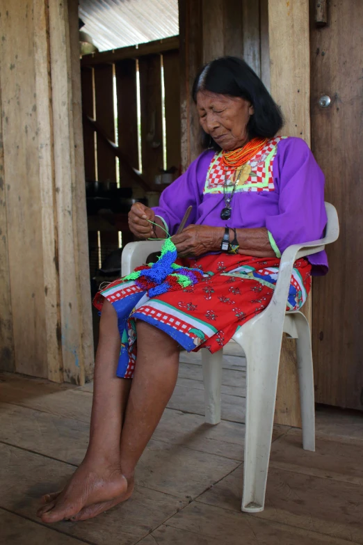 a woman sitting in a chair weaving on a piece of string