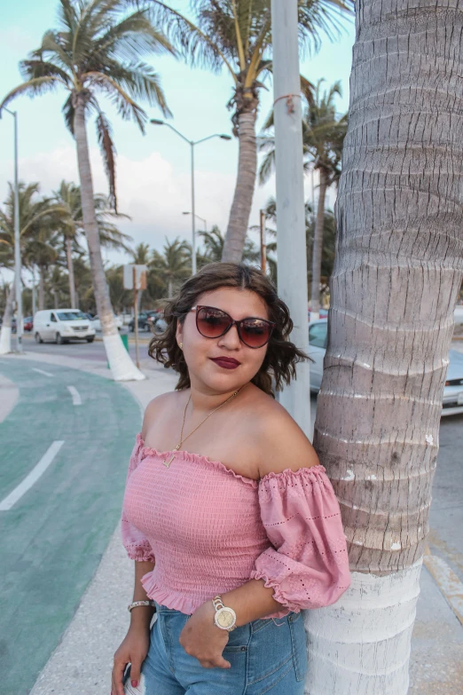 a woman in an off the shoulder top is leaning against a palm tree