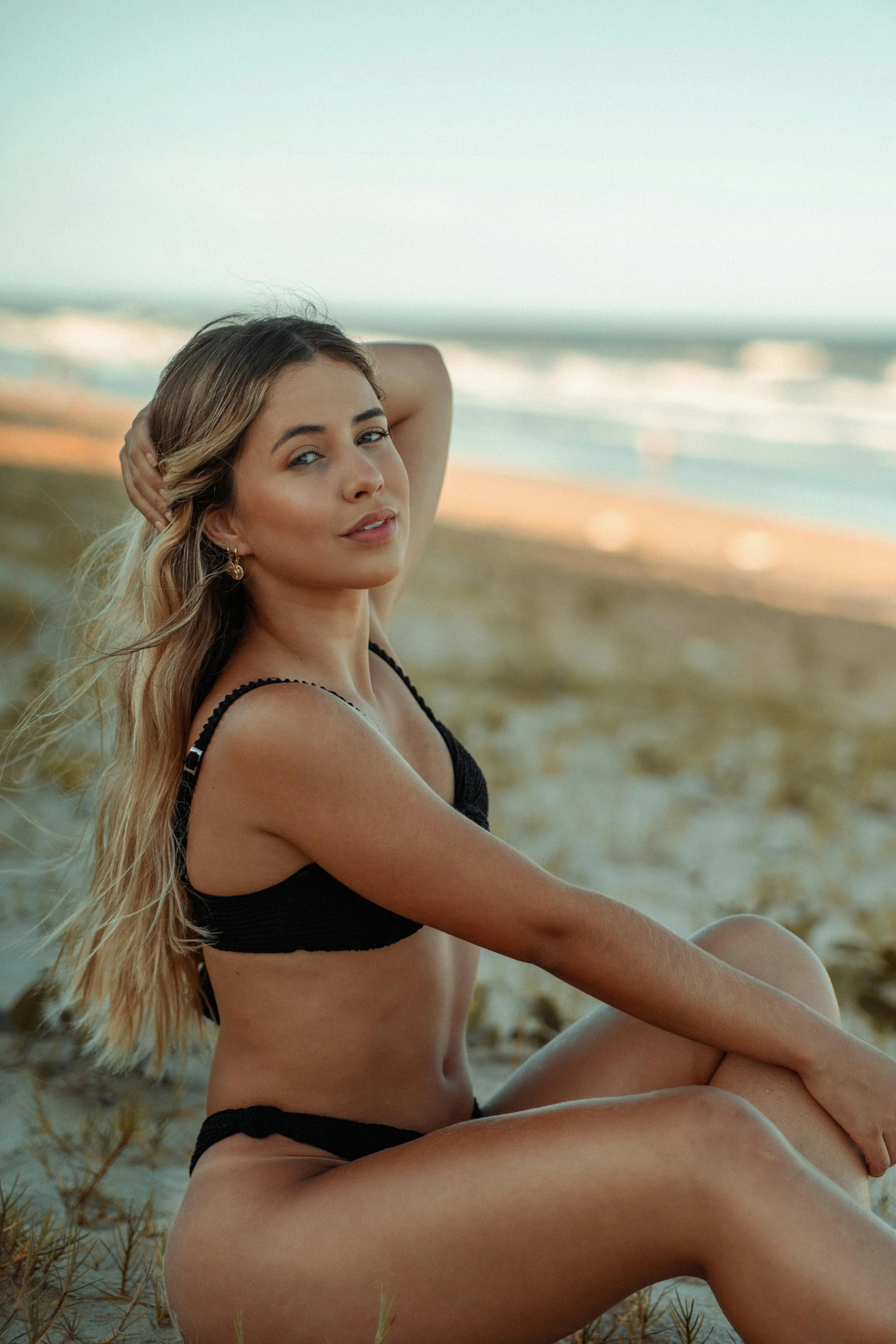 a woman in a black bikini sitting on the beach