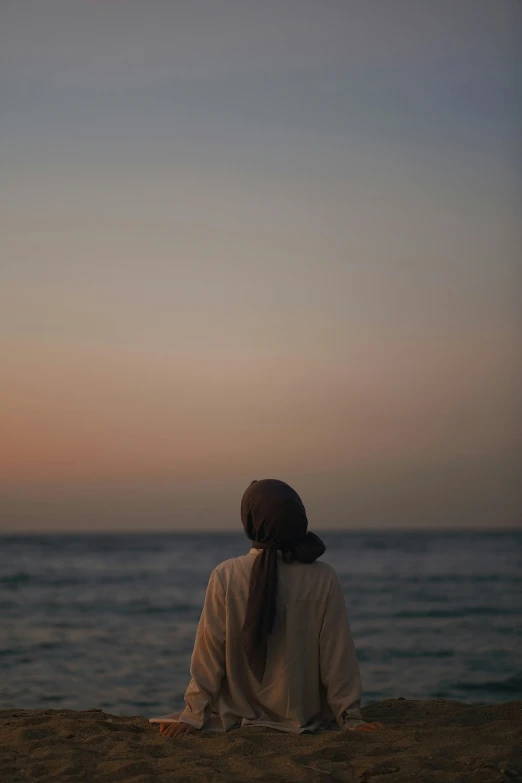 a woman is sitting in the sand by a body of water