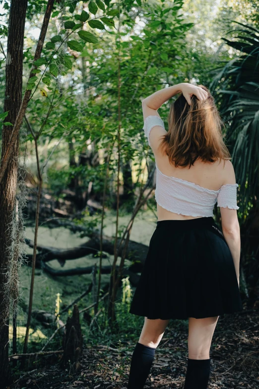 woman in a short skirt, boots and top looks at plants in a forest