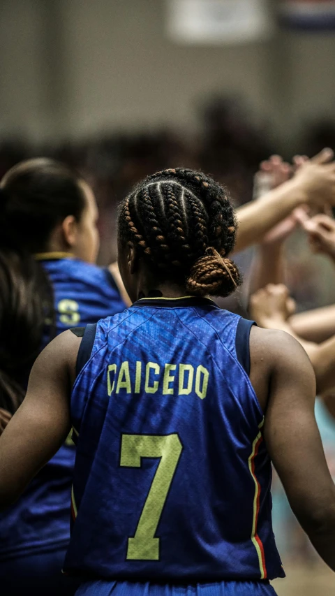 women's basketball players in a huddle with one of their hands raised