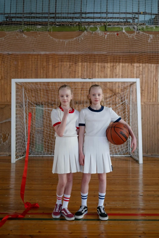 two girls wearing tennis clothes holding a basketball