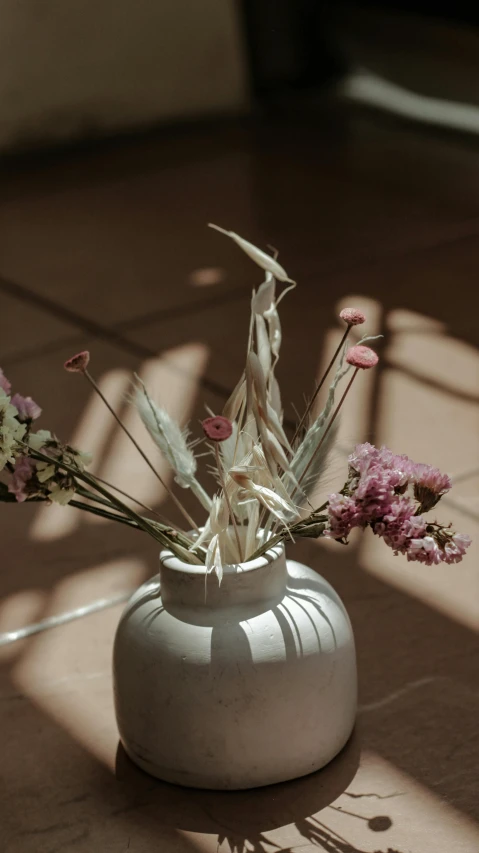 a white vase sitting on the ground holding pink and white flowers