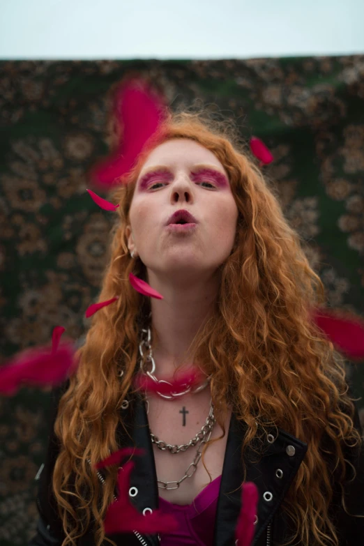 a woman with red hair blowing and blowing rose petals