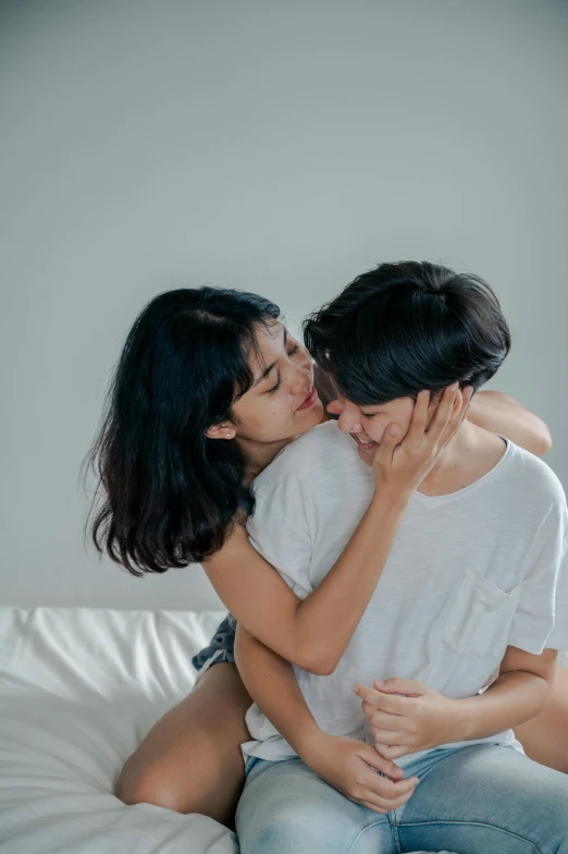 two people sitting on a bed kissing each other