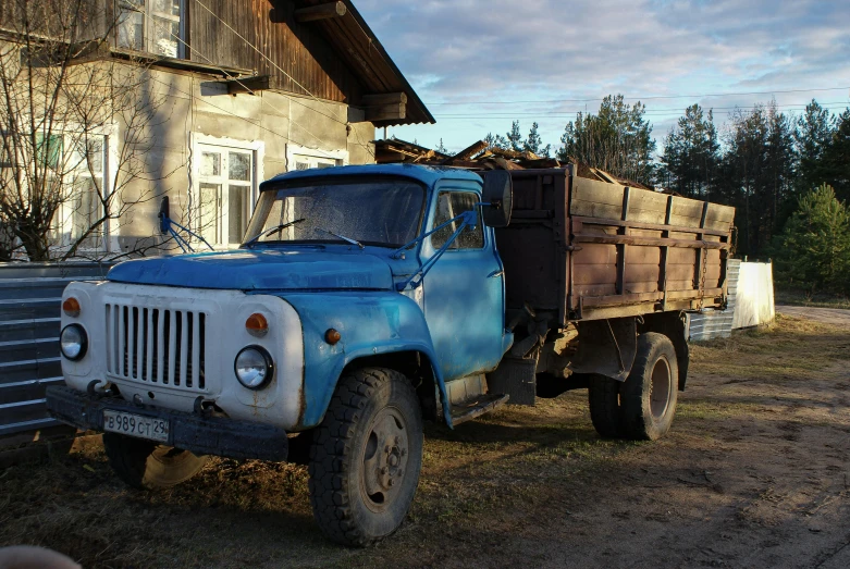 an old blue truck is parked in front of a house