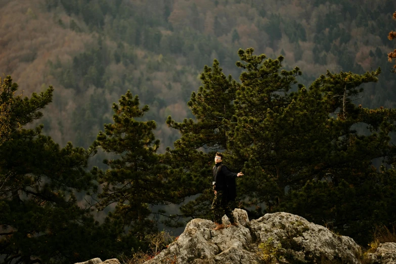 two people stand on top of a hill while one person stands on a cliff