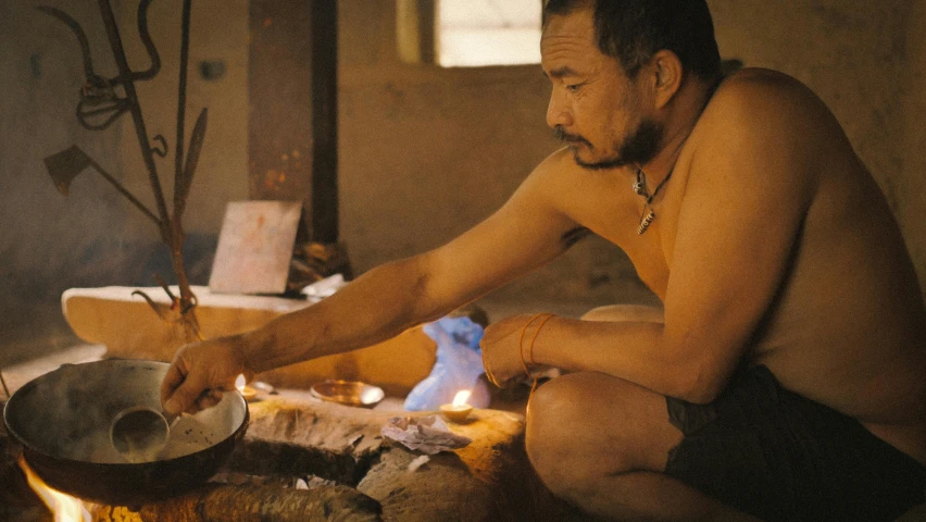 a man sitting in front of an open fire cooking soing