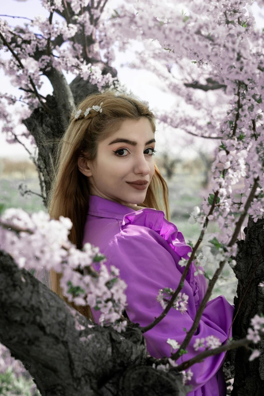 a woman poses near some flowers on a tree