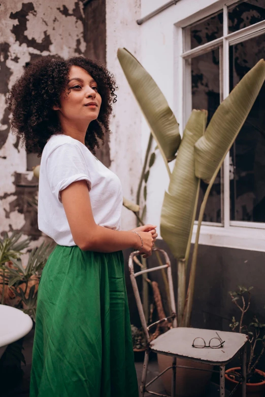 the girl is standing near a plant in front of the window