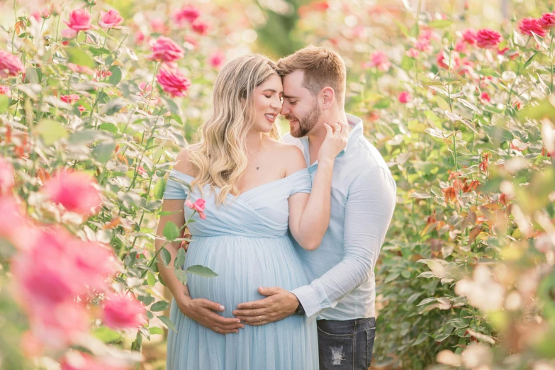 a pregnant couple standing in flowers, one of them holds the other