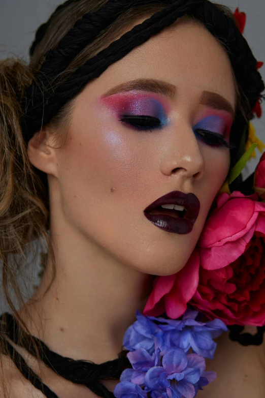 a woman with purple, red and blue eyeliners holding pink flowers