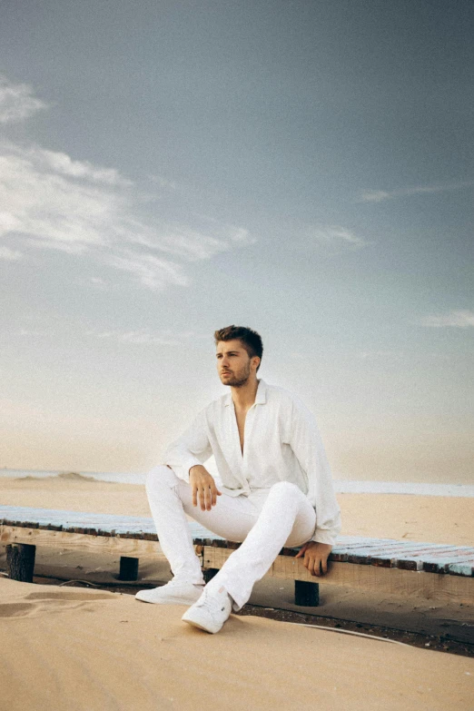 a man sitting on the beach in white clothing