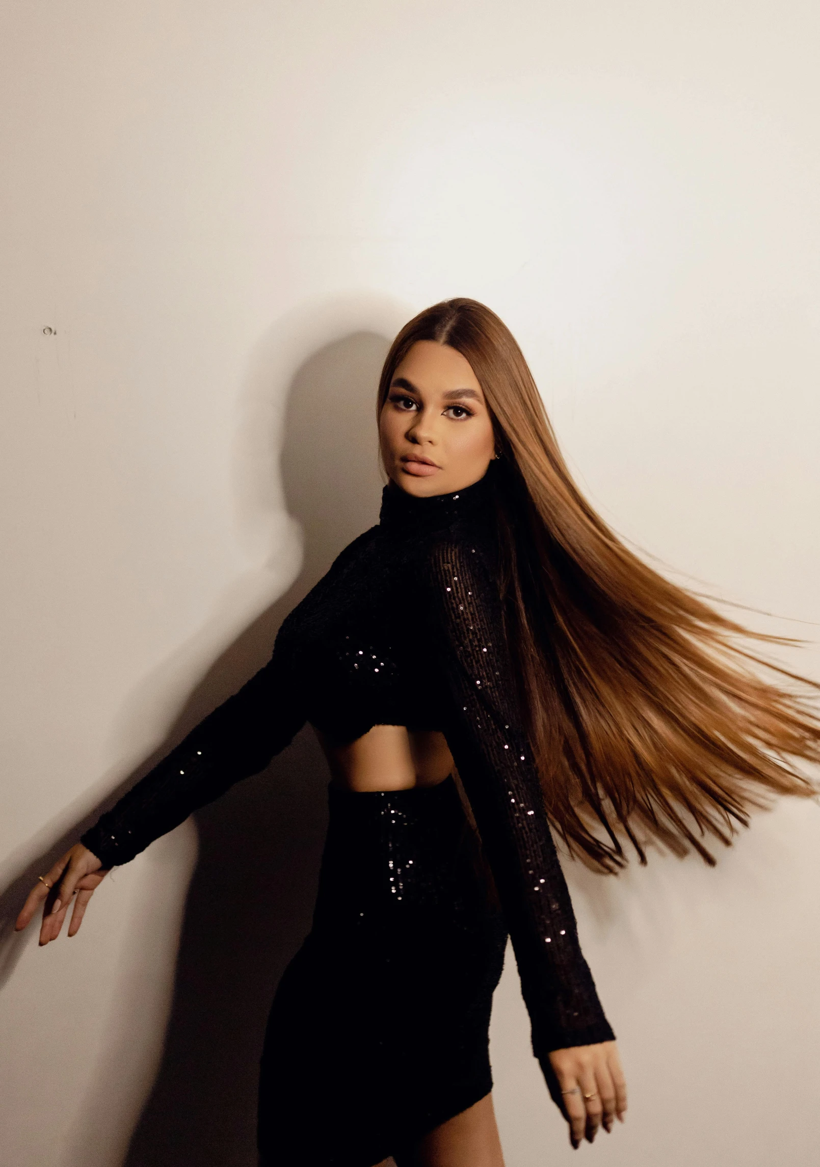 a woman with long hair and black stockings standing against a white wall