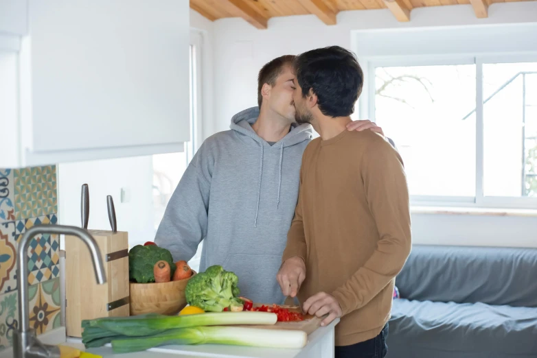 two men are standing near the counter and one is kissing the other