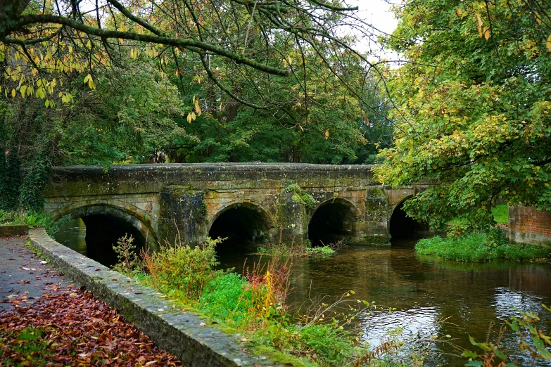 a stone bridge spanning over a river next to trees