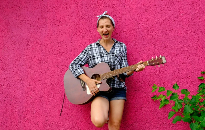 a woman plays a guitar against a pink wall