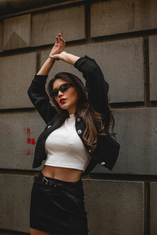 a woman standing near a wall with her hands behind her head