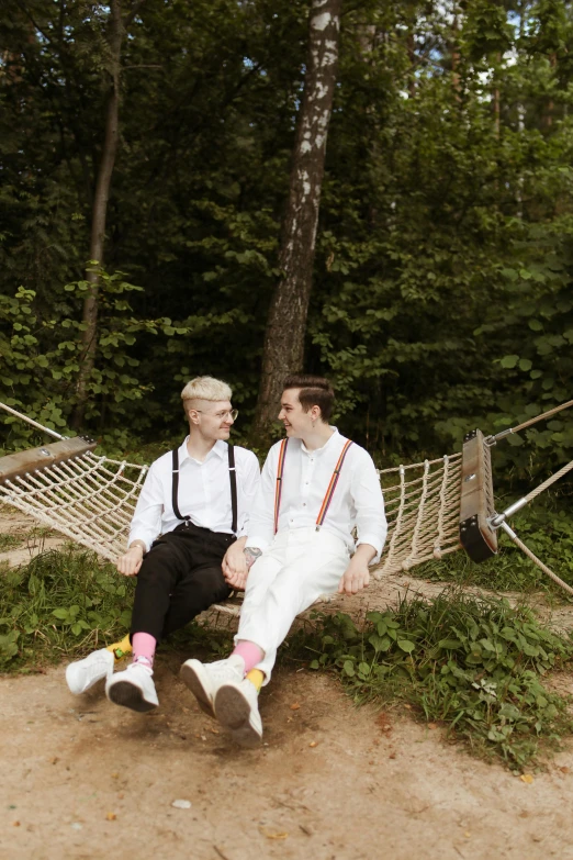 a married couple in white are sitting on a hammock