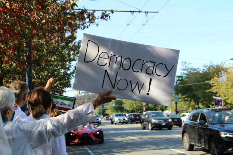 two people holding a sign that says democracy now