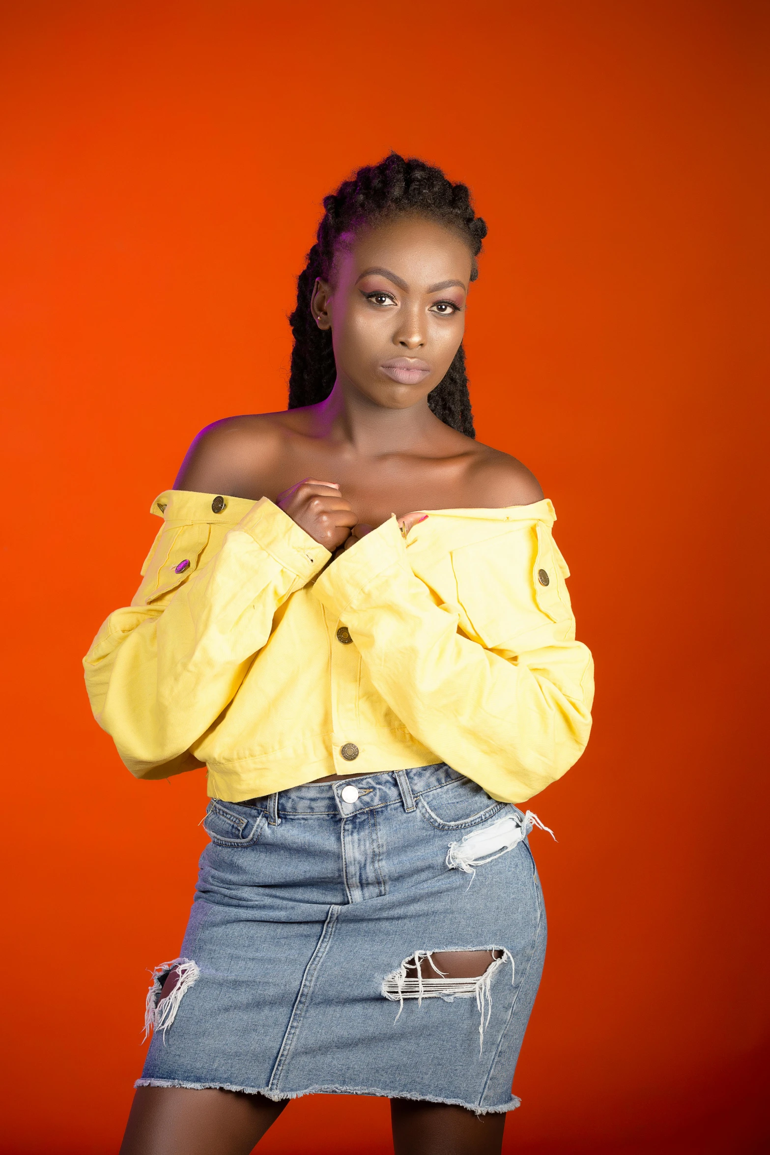 woman in yellow jacket, denim skirt and short legs with orange background