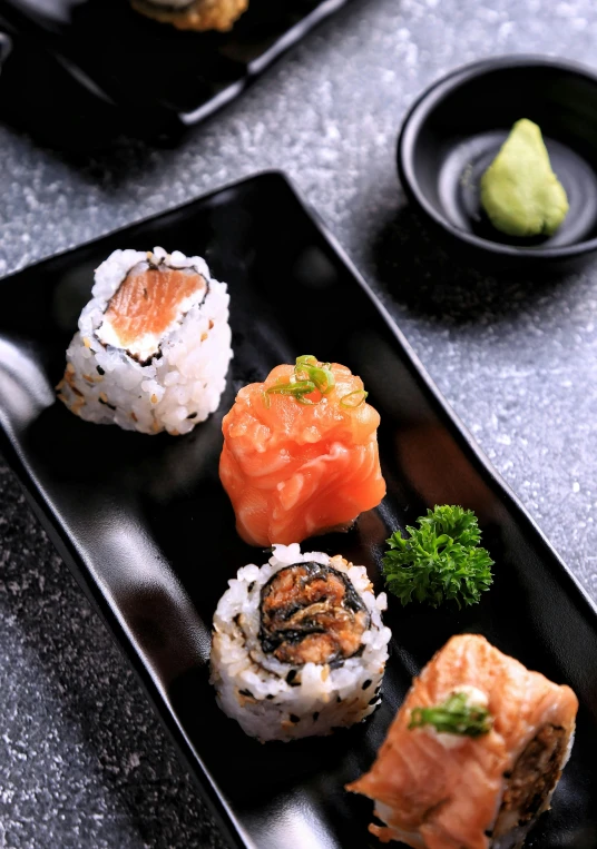 a black plate topped with sushi and broccoli