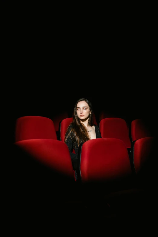 a woman is sitting in the middle of a red cinema auditorium
