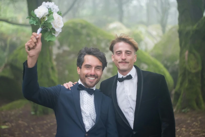 two men wearing tuxedos pose for the camera