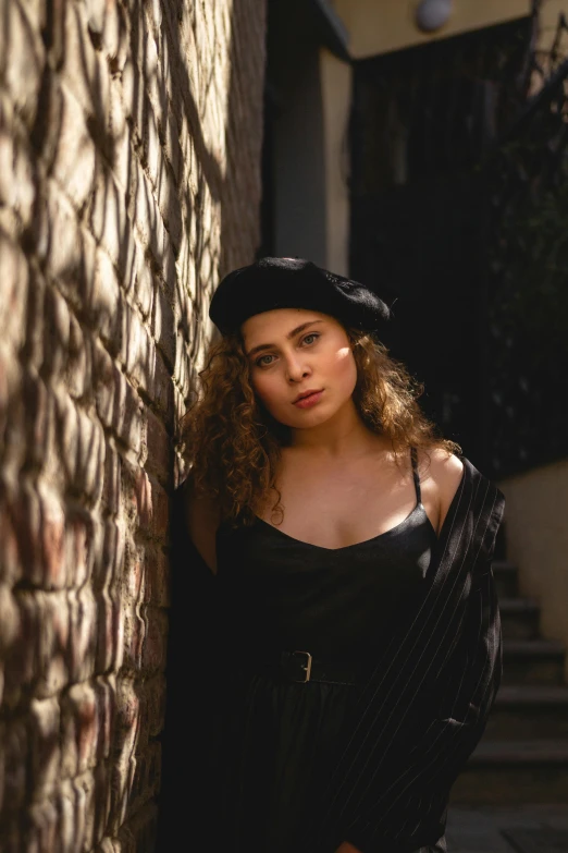 a beautiful woman wearing a hat leaning on a wall