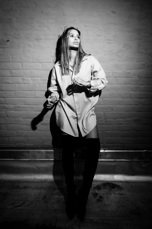 a woman posing on the side of a white brick wall