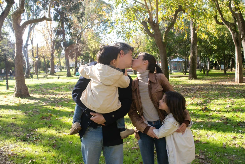 three children and two adults are standing in front of the trees and have their faces up to the park's air