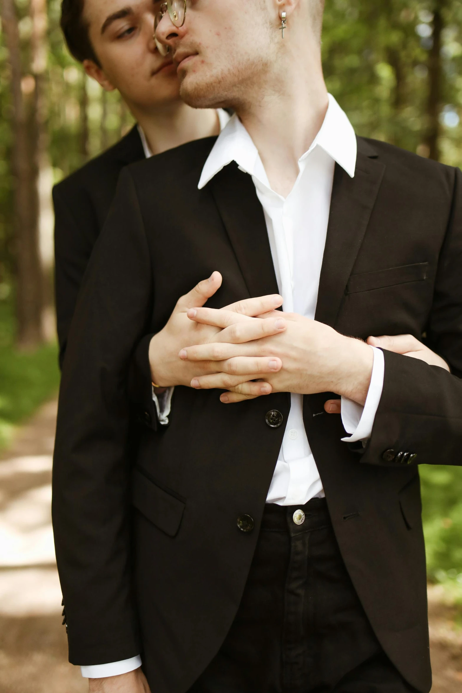 two young men in black suits are kissing in the forest